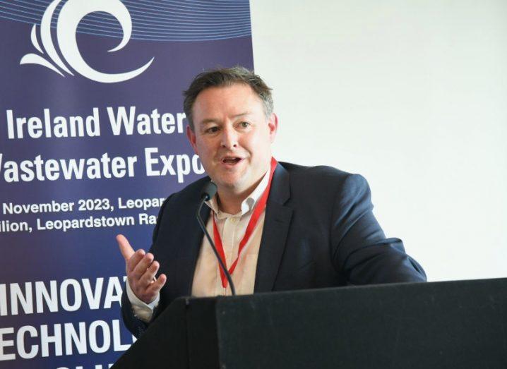 A man in a suit speaking in front of a podium. He is Colm Lynch, the CEO of Aquamonitrix.