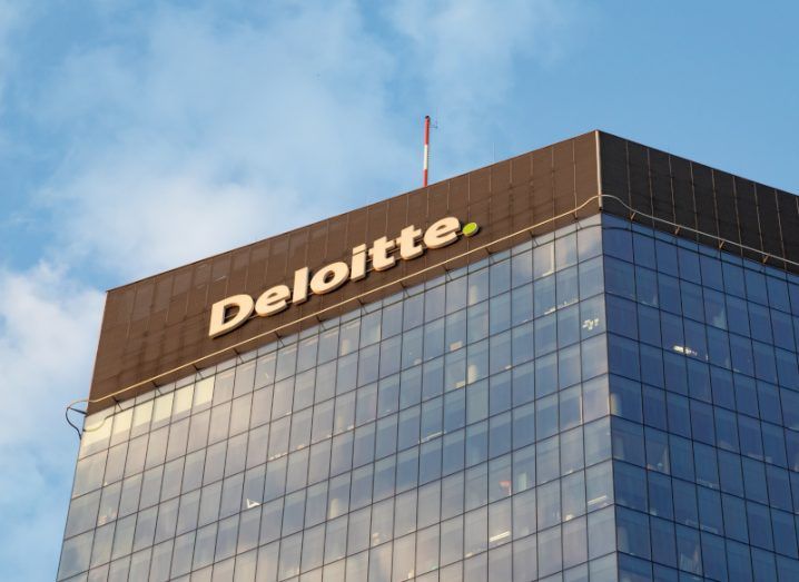 A large glass building with the Deloitte logo at the top against a blue sky.