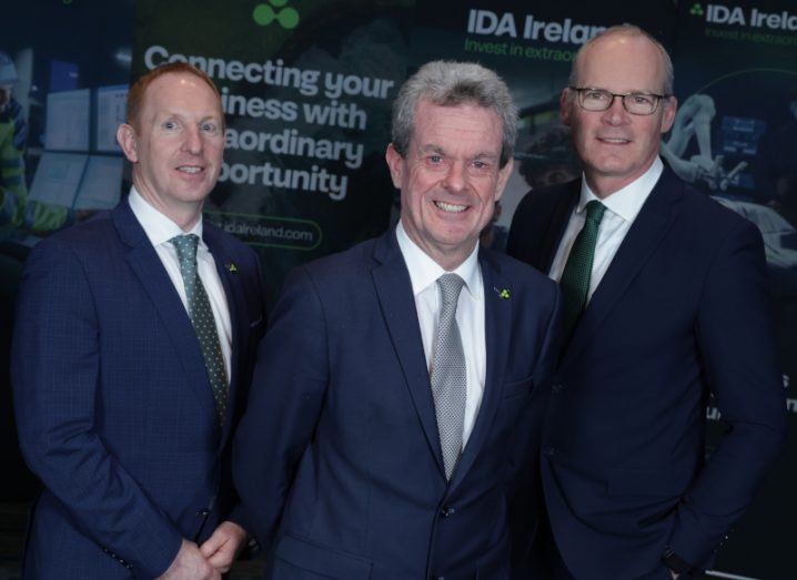 Feargal O'Rourke of IDA Ireland standing in front of a large poster wall with IDA Ireland branding flanked by IDA Ireland CEO Michael Lohan and Minister Simon Coveney.