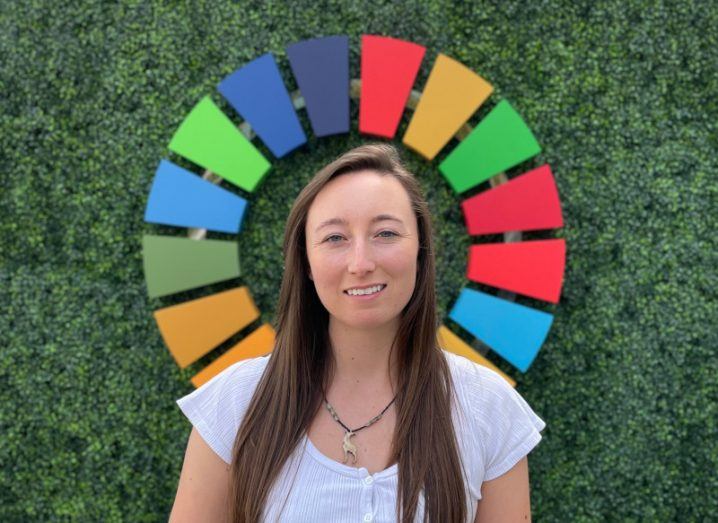 Ciara Judge standing against a background with a green hedge and a multi-coloured wheel.