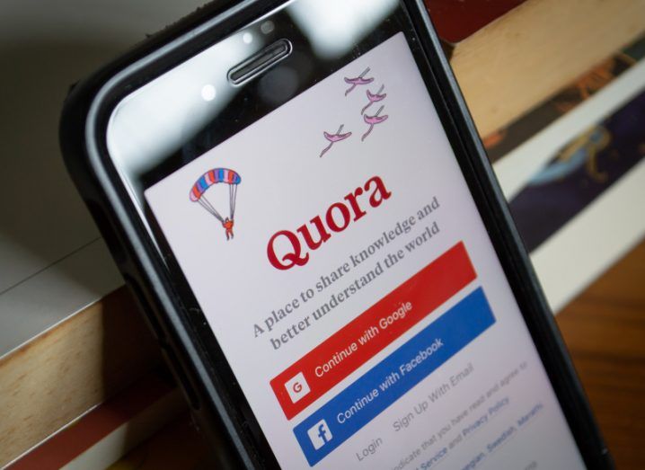 The Quora login screen on a phone leaning up against a wooden surface.