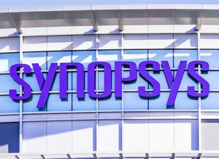 A close-up of the purple Synopsys name/logo on a glass-fronted building.