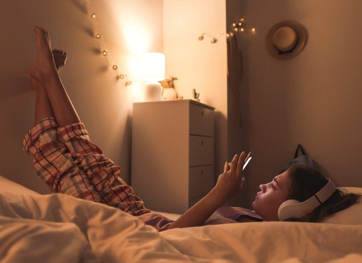 Teenage girl using a smartphone in what appears to be her bedroom at night.