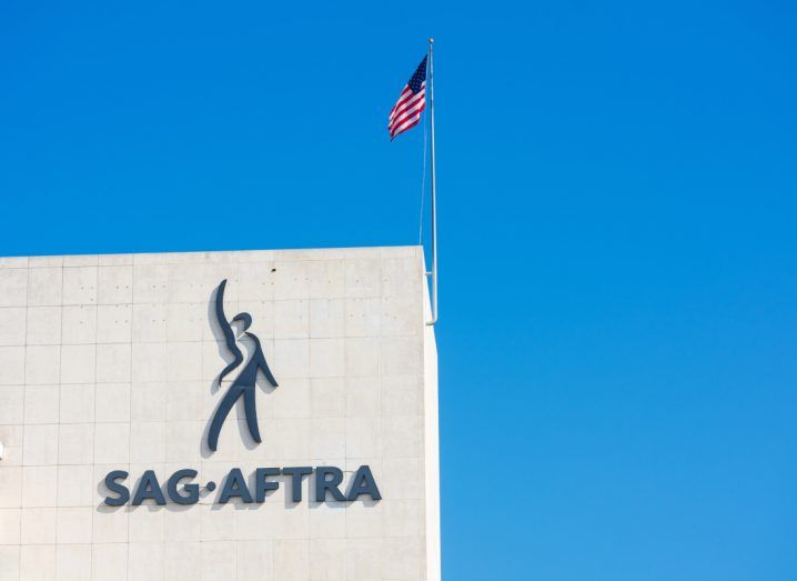 SAG-AFTRA logo on a building with the blue sky in the background. The US flag is hoisted on the building.