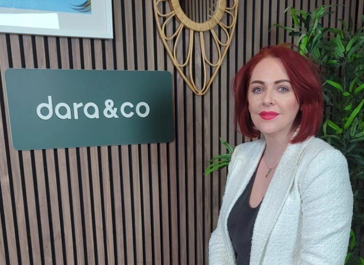 Headshot of a woman standing in front of a wall that has the Dara and Co logo on it.