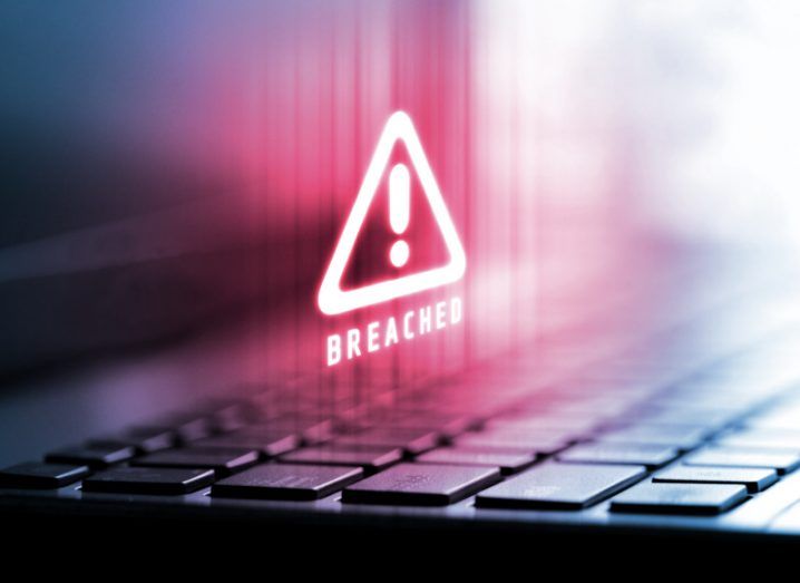 A digital image of a computer keyboard where a hologram of a red warning sign with the word 'breached' hovering underneath it.