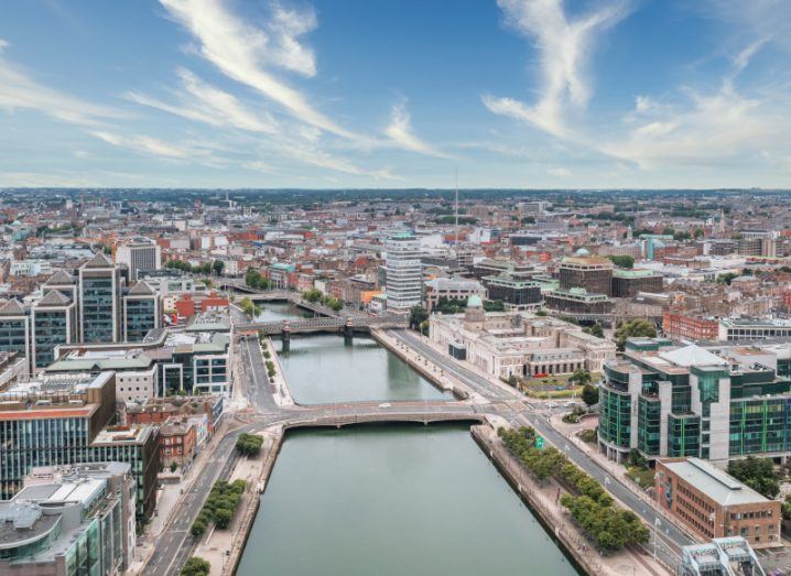 A bird's eye view of Dublin with the river Liffey in the centre and a blue sky with some small clouds above.