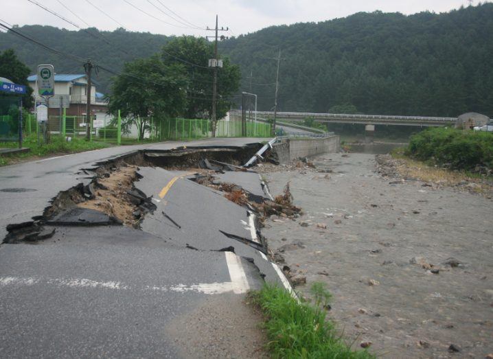 A road that has been partially destroyed by extreme flooding alongside a river.