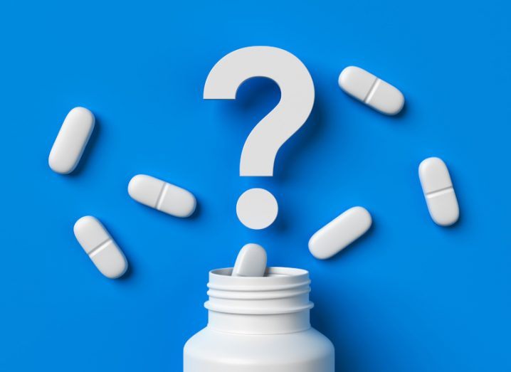 Plastic medical container and white capsule pills with question mark on blue background.