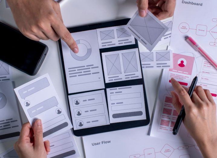 An aerial view of two people working on a UX design with note cards. There is also a phone and a table on the table.