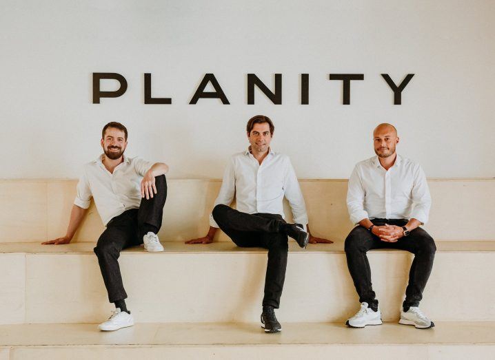 Three men seated on a platform with the Planity logo on the wall behind them.