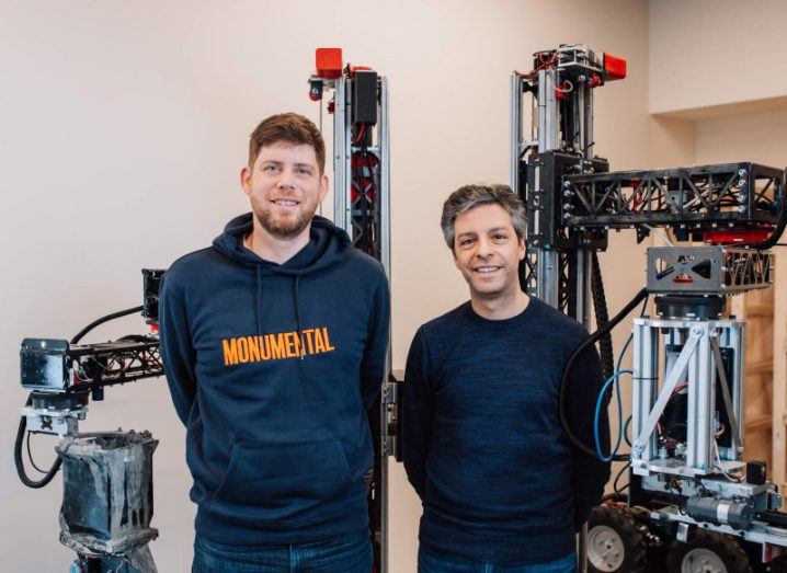 Two men standing in a small room with robots behind them. They are the co-founders of Monumental.