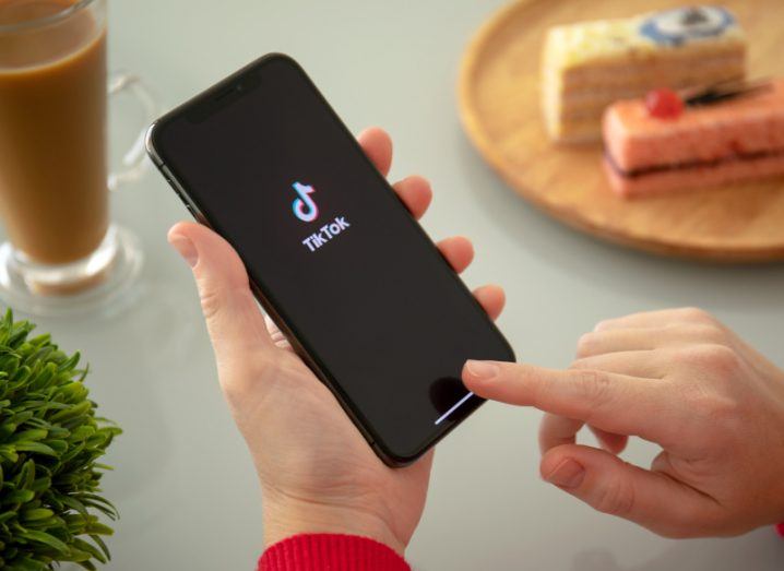 The TikTok logo on a smartphone screen. The phone is held in a person's hand above a table.