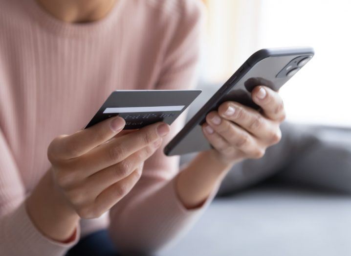 A woman holding a mobile phone in one hand and a credit card in another hand. Used to show the concept of online banking scams.