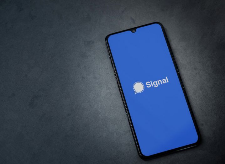 The Signal app logo on a smartphone screen. The phone is laying on a dark grey surface.