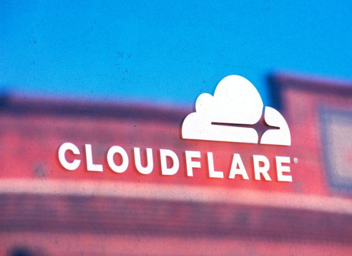 The Cloudflare logo on a reflective surface with a building visible in the background.