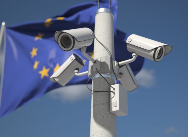 A pole with multiple security cameras on it and an EU flag in the background.