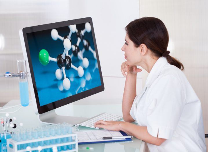 A woman sitting at a desk and looking at a computer screen that has a close-up image of molecules on it.