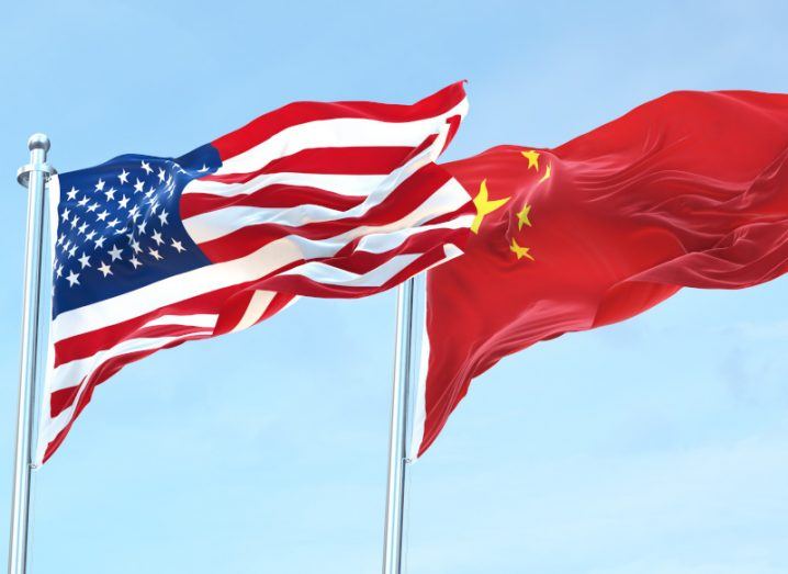The US flag and the Chinese flag on flag poles next to each other, with a blue sky in the background.