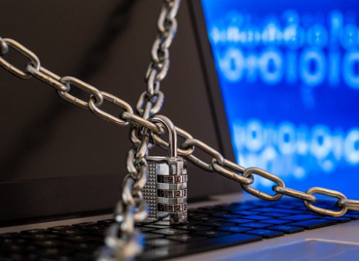 A lock and chains around an open laptop, with blue binary code in the background behind the laptop. Used to represent the concept of cybercrime.