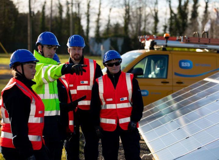 A group of people in high-vis jackets standing by a row of solar panels with an ESB van in the background.