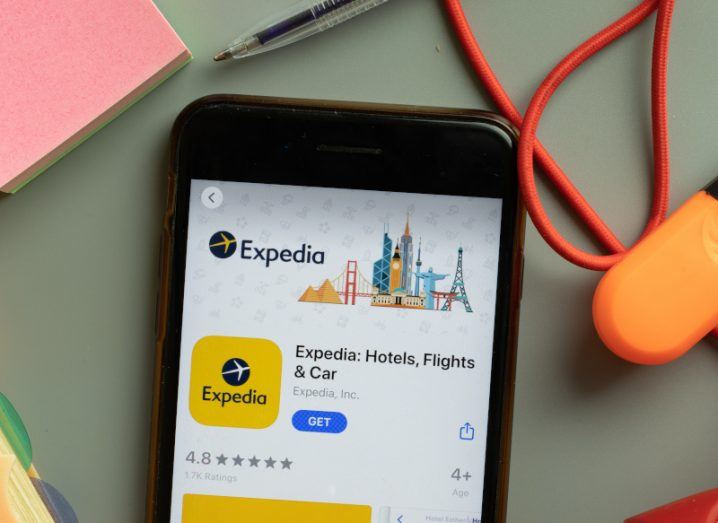 A phone on a table surrounded by stationery. The phone has the Expedia app open on the screen.