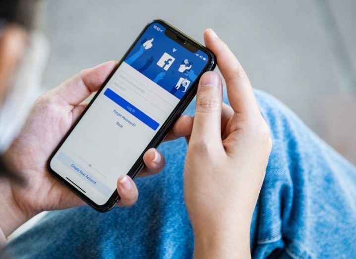 A person holding a smartphone with the Facebook login screen open.