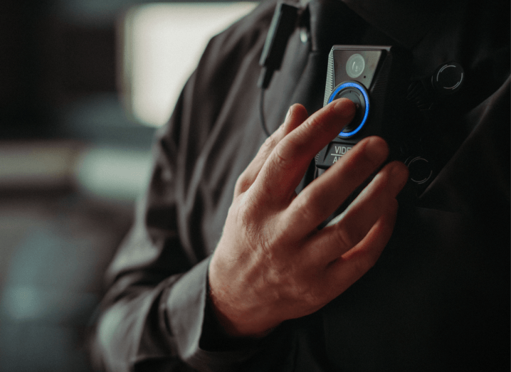 A man dressed in security uniform presses a button on a bodycam attached to his chest.