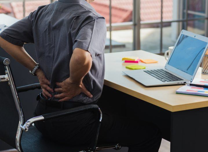 Man sitting at his desk holding his lower back presumably because of pain.