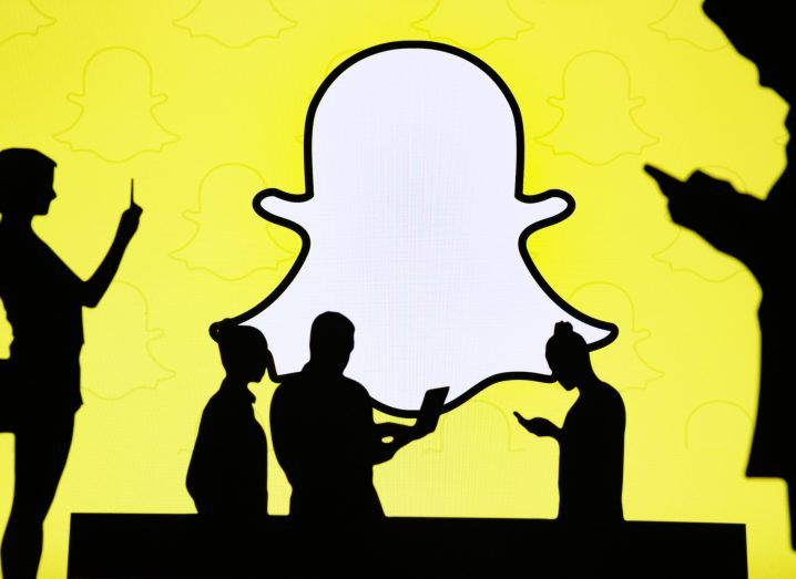 Silhouettes of people using their phones against the backdrop of the Snapchat logo.