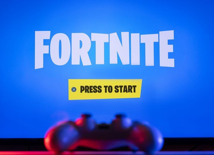 Fortnite start screen on a TV display with a remote control in the foreground.