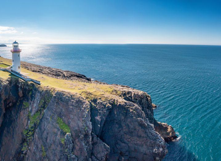 A lighthouse on a cliff in Donegal looking out onto the beautiful clear blue ocean and sky.