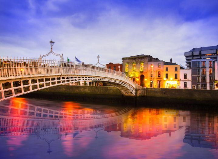 A picture of the Ha'penny Bridge in Dublin at dusk, with streetlights reflecting off of the River Liffey,