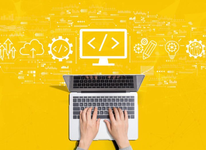 An aerial shot of hands typing on a laptop against a yellow background with white symbols of software development above.