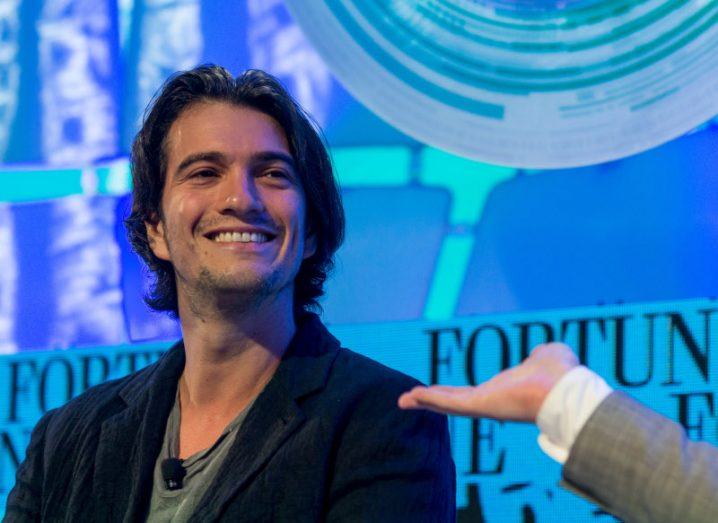An image of WeWork co-founder and former CEO Adam Neumann, sitting on a stage.