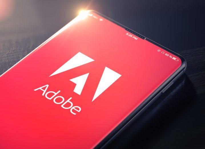 The Adobe company logo on the screen of a smartphone laying on a dark surface.