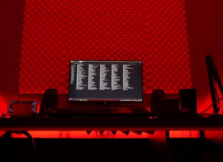 A computer with code on the screen, on a desk in a red room. Used as a concept for cyberattacks from LockBit.