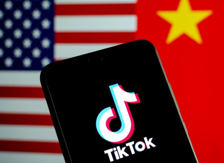 The TikTok logo on a smartphone screen, with a US flag and a Chinese flag behind it.