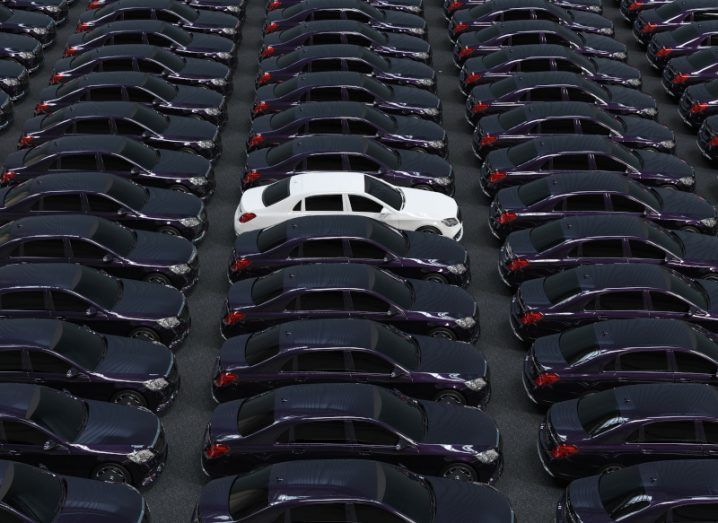 A white car parked and surrounded by black cars, to show the concept of a change in fleet management.
