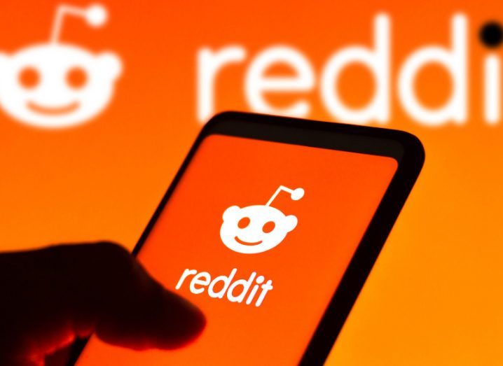 The Reddit logo on a smartphone screen and on a wall in the background.