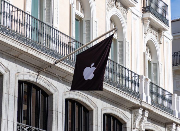 The Apple company logo on a black flag hanging on the side of a building.