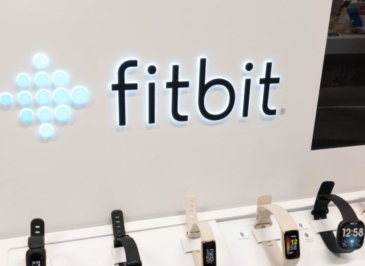 The Fitbit logo on a wall with multiple Fitbit devices on display below the logo.
