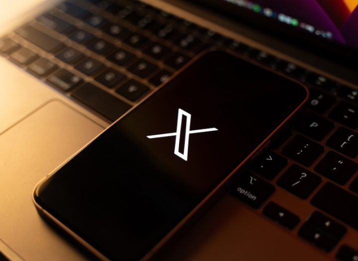 The X logo on the screen of a smartphone, which is laying on a laptop.