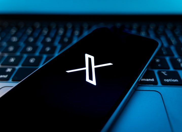 The X logo on the screen of a smartphone that is on top of a laptop keyboard.