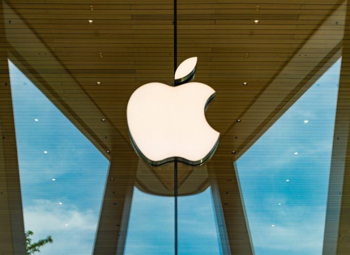 The Apple logo on the window of a building, with a part of the building reflected in the window.