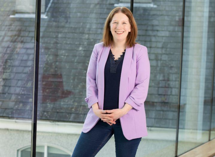 Dr Lynette Keeney standing against a large glass window with a building visible out the window in the background.