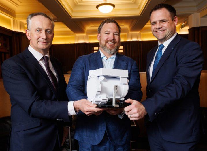 Three men in suits hold a white piece of technical equipment. They are Leo Clancy, John Mackey and Minister of State Neale Richmond.
