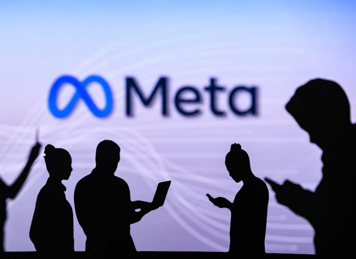 Meta logo on a wall with silhouettes of people in the foreground.