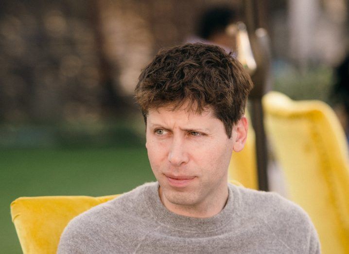 Sam Altman looking off to the side while sitting in a yellow chair.