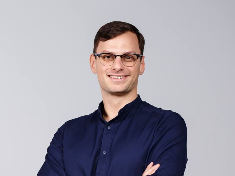 A man wearing glasses and a dark blue shirt smiles at the camera with his arms folded. He is Victor Chircu.
